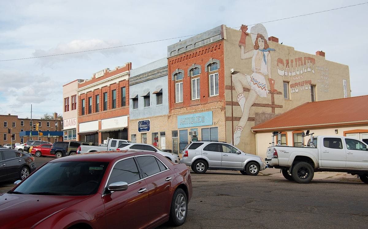 A street of low brick buildings with a painted mural, cars parked in front