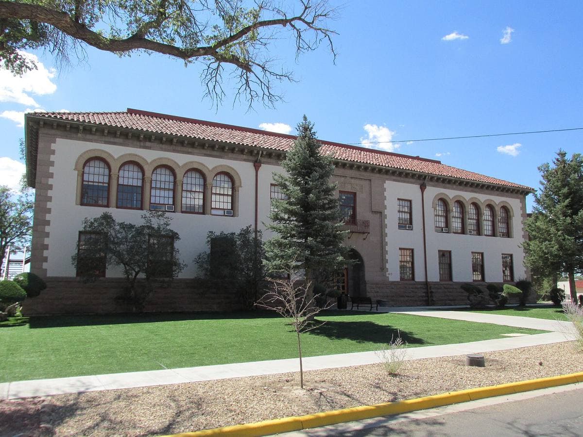 A pale stucco university building with arched windows and a red-tiled roof