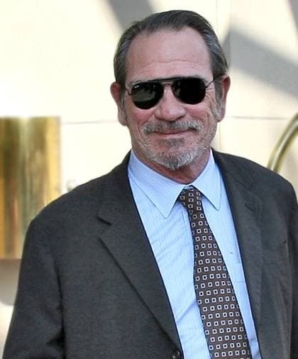 Tommy Lee Jones in sunglasses, suit and patterned tie, smiling