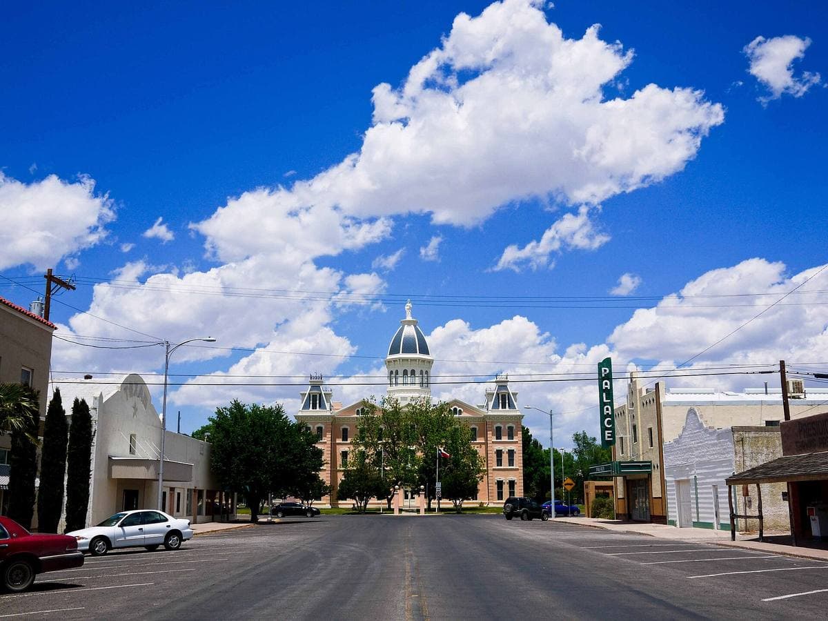 A wide main street leading to a domed courthouse under big clouds