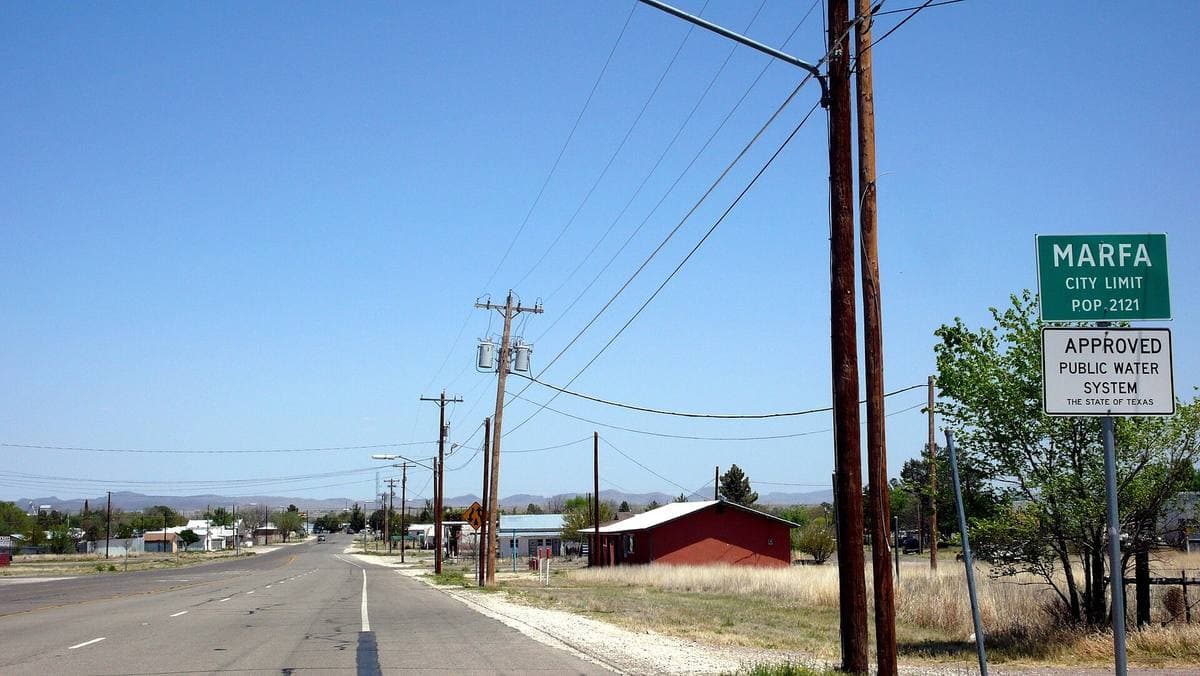 A straight highway running into a small town under a wide pale sky, power poles on one side
