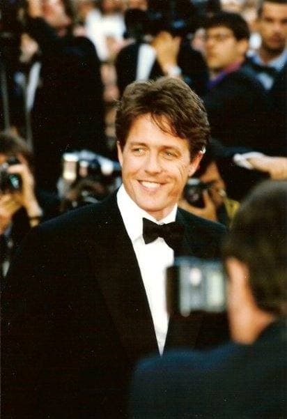 Hugh Grant in black tie, smiling, among photographers at Cannes