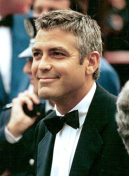 George Clooney in a dinner jacket and bow tie, smiling, on the Cannes steps