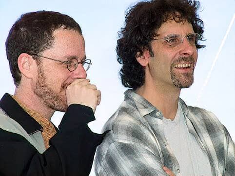 Ethan Coen, hand to his mouth, beside a laughing Joel Coen in a checked shirt