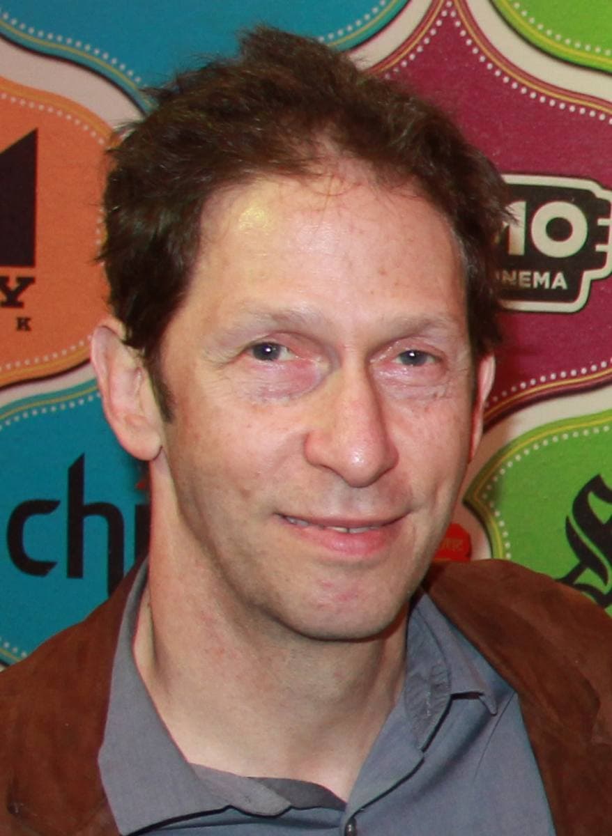 Tim Blake Nelson smiling, close up, in front of a colourful festival backdrop