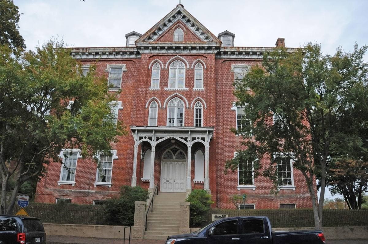 A tall red-brick Gothic Revival building with a white porch, framed by trees