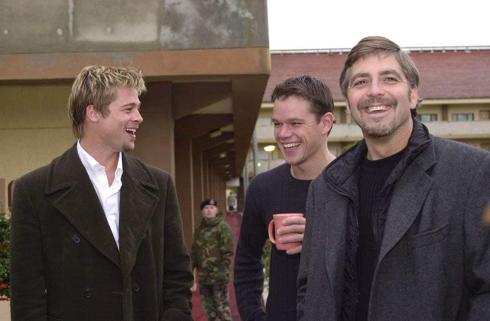 Brad Pitt, Matt Damon and George Clooney in dark coats, laughing together outdoors