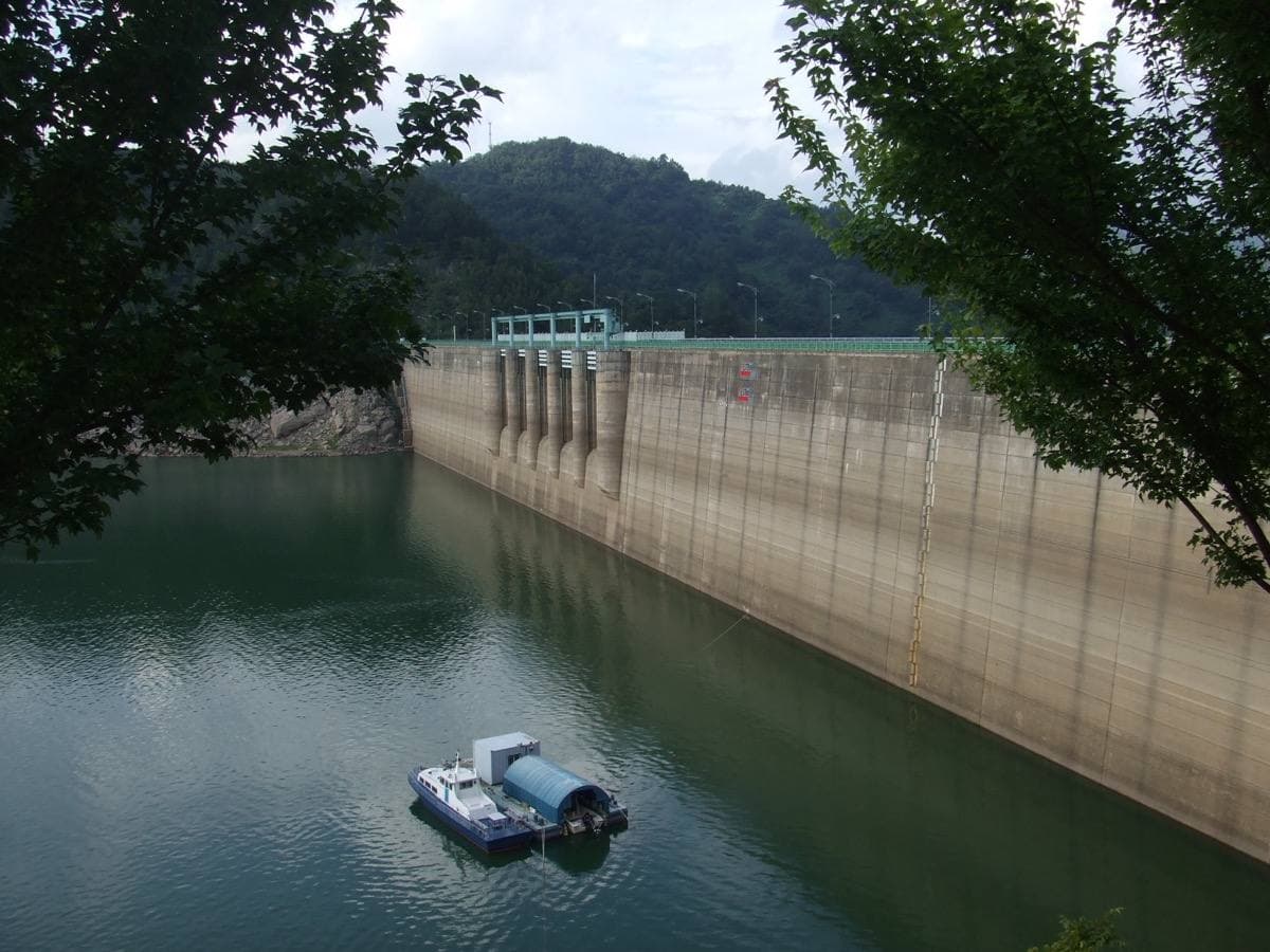 A concrete dam holding back a lake among green hills