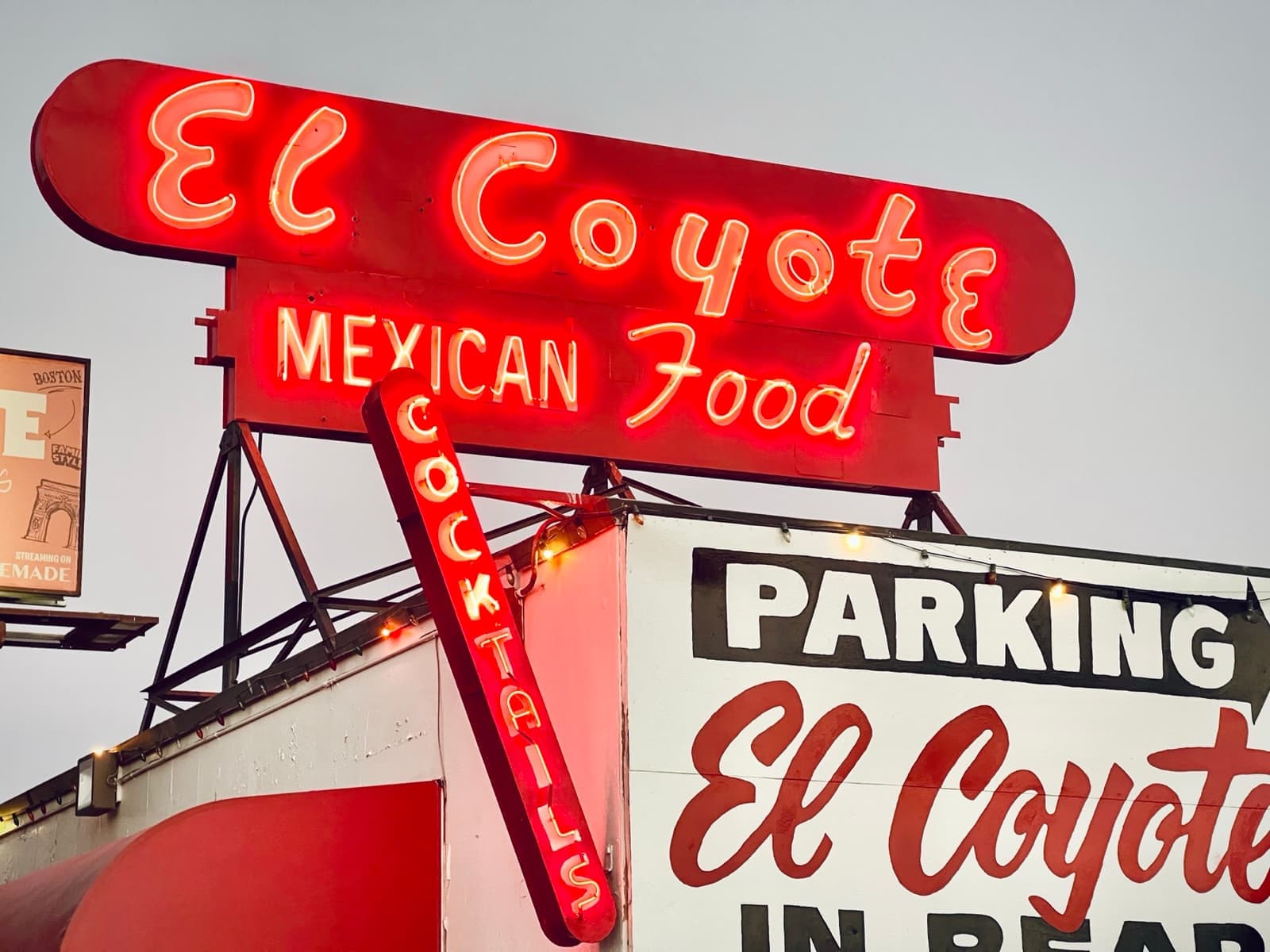 A red neon El Coyote Mexican Food sign lit against a grey dusk sky