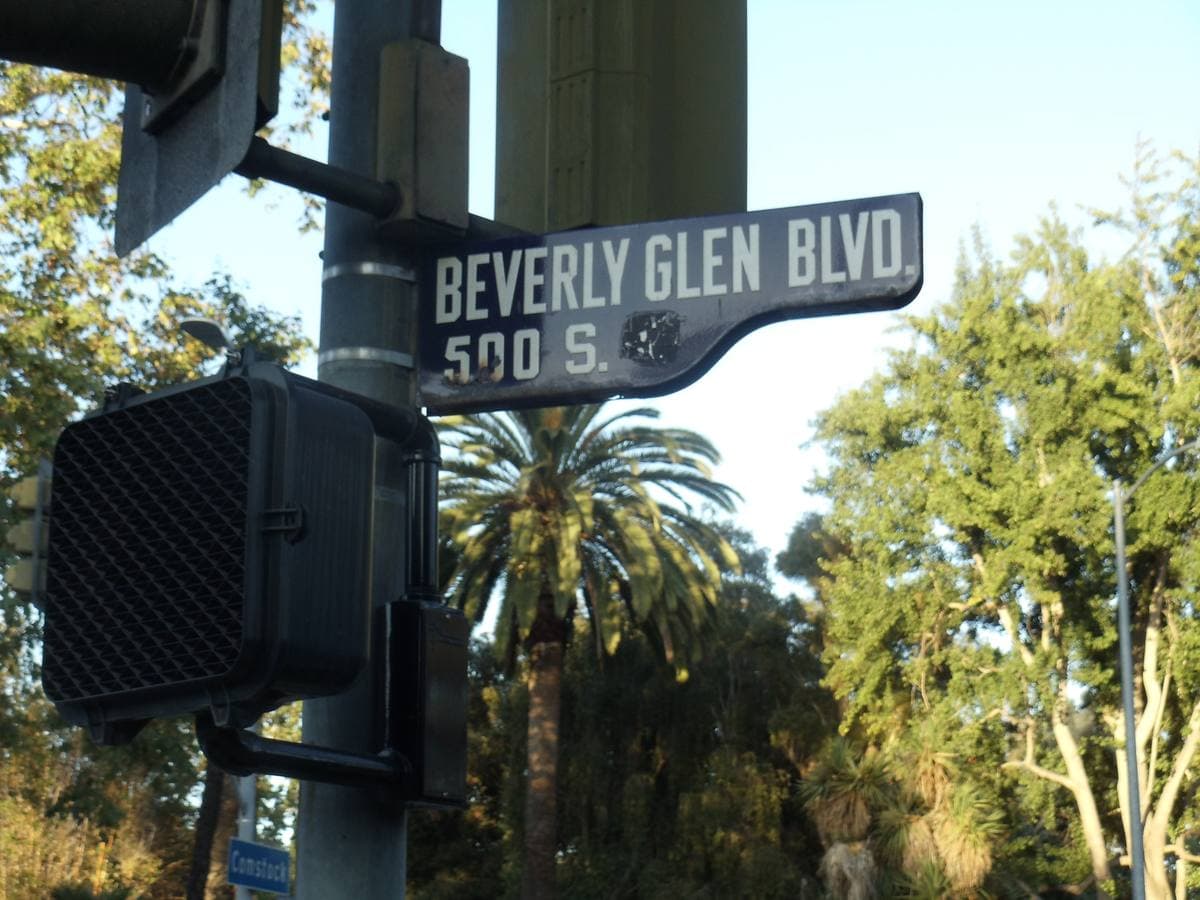 A green Beverly Glen Blvd street sign against trees and palms