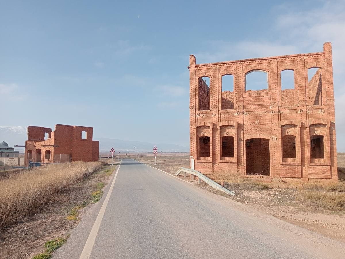 Roofless red-brick facades with empty window openings beside a straight country road
