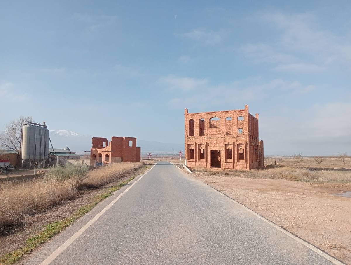 A tall brick facade with arched openings standing alone beside a road on the plain