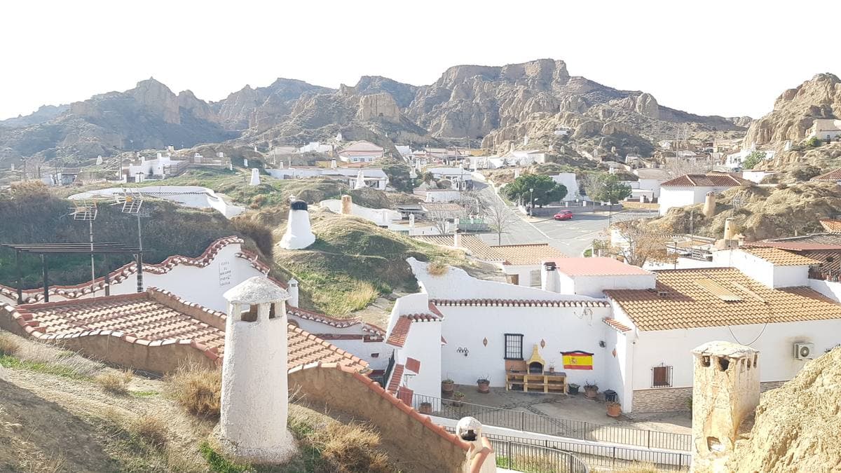 White chimneys of cave houses rising from the ground among low hills in Guadix