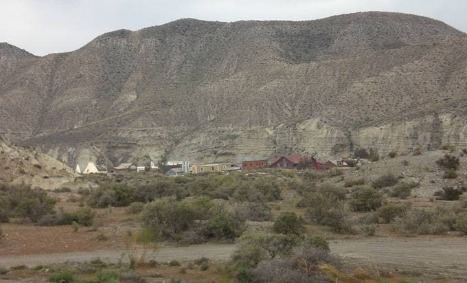 A small cluster of wooden western buildings at the foot of a bare grey hillside