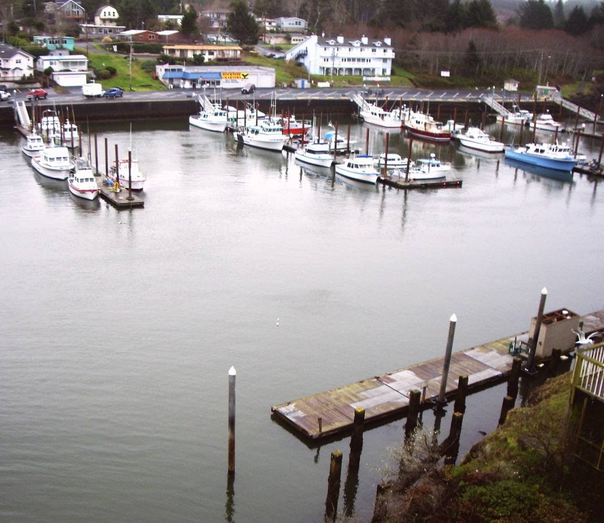 A calm, small harbour with boats at docks under wooded banks