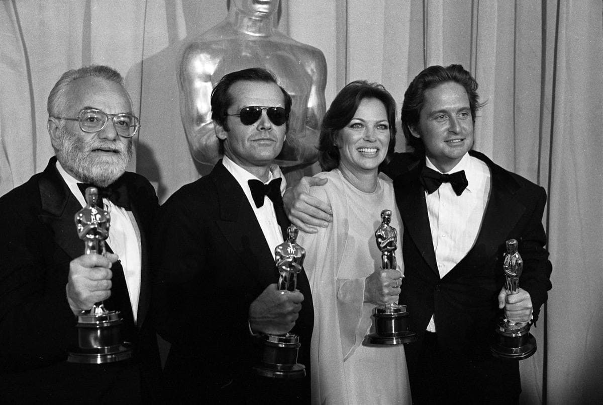 Two men in tuxedos, a woman in a pale gown and a third man, each holding an Oscar statuette