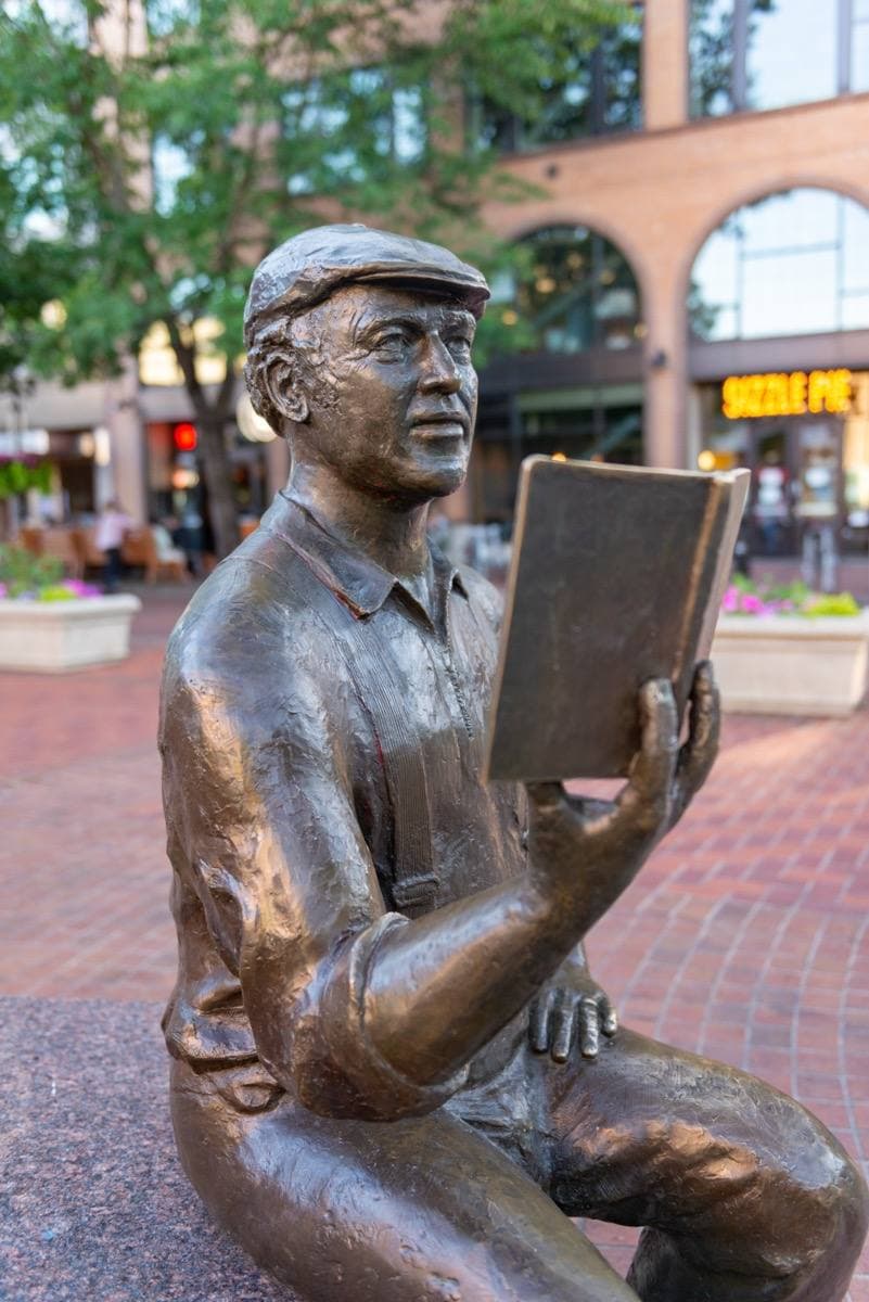 A bronze of Ken Kesey seated on a bench reading to three children