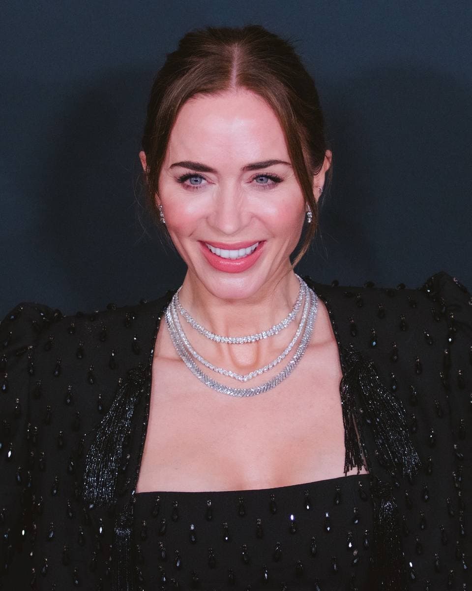 Emily Blunt in a black sequinned top and layered silver necklaces, smiling