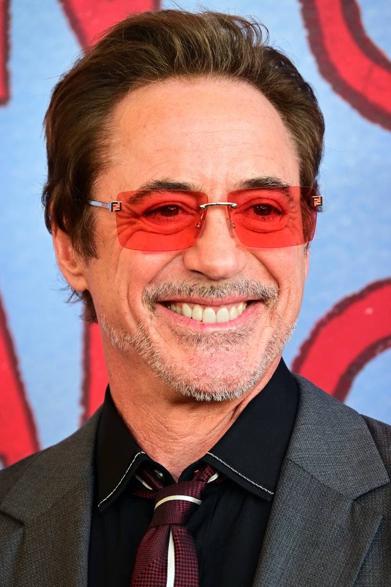 Robert Downey Jr. in tinted rimless glasses and a grey jacket, smiling