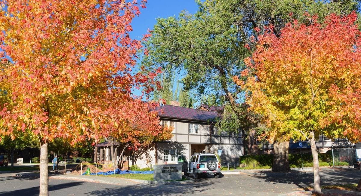 A long log building glimpsed between trees in red and orange autumn leaf