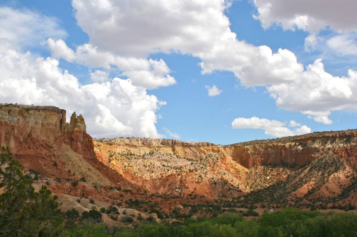 Layered red and cream sandstone cliffs above green scrub, under white clouds