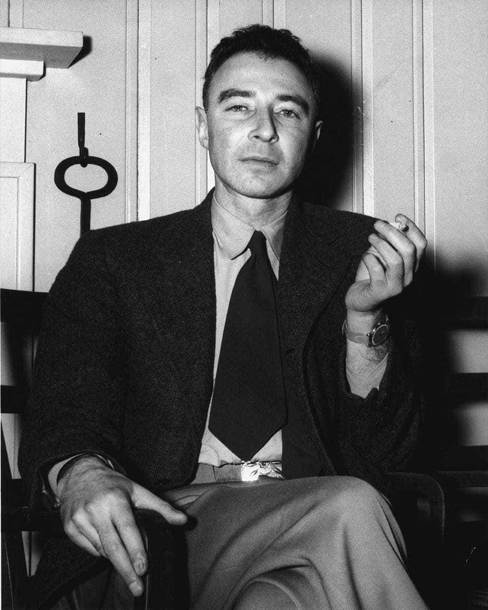 Oppenheimer seated in a suit and tie, holding a cigarette, in a black-and-white photograph