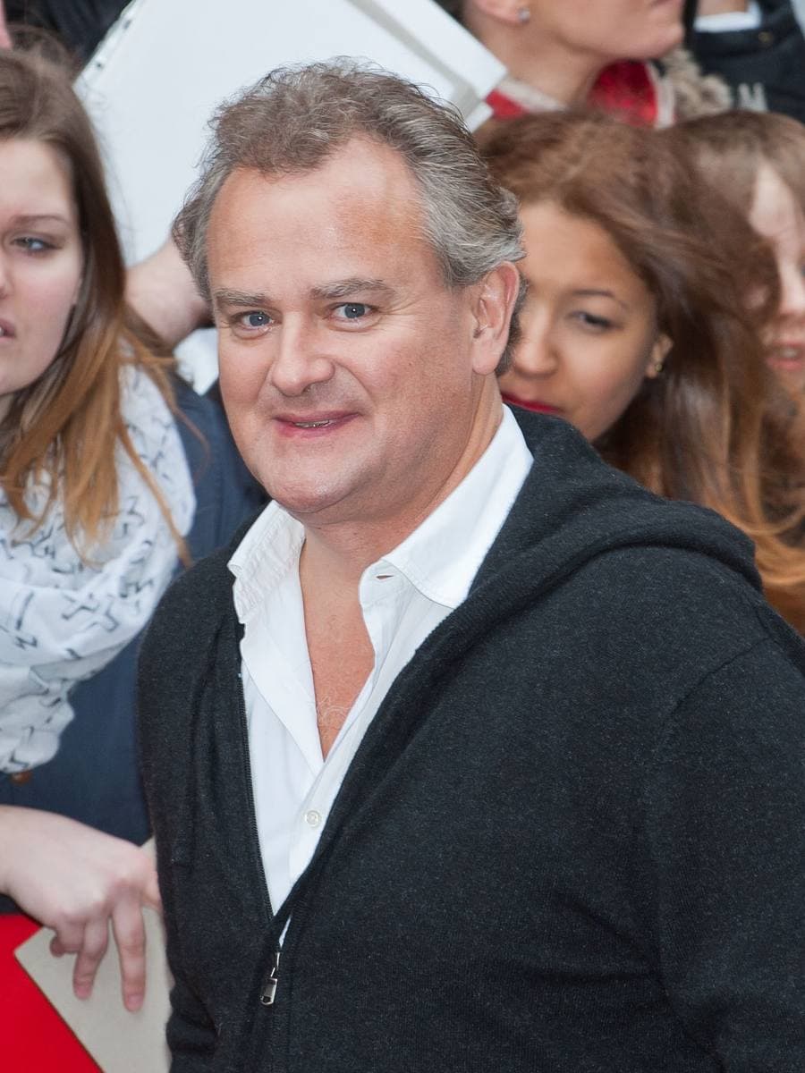 Hugh Bonneville in a dark zip jacket and white shirt, in a crowd