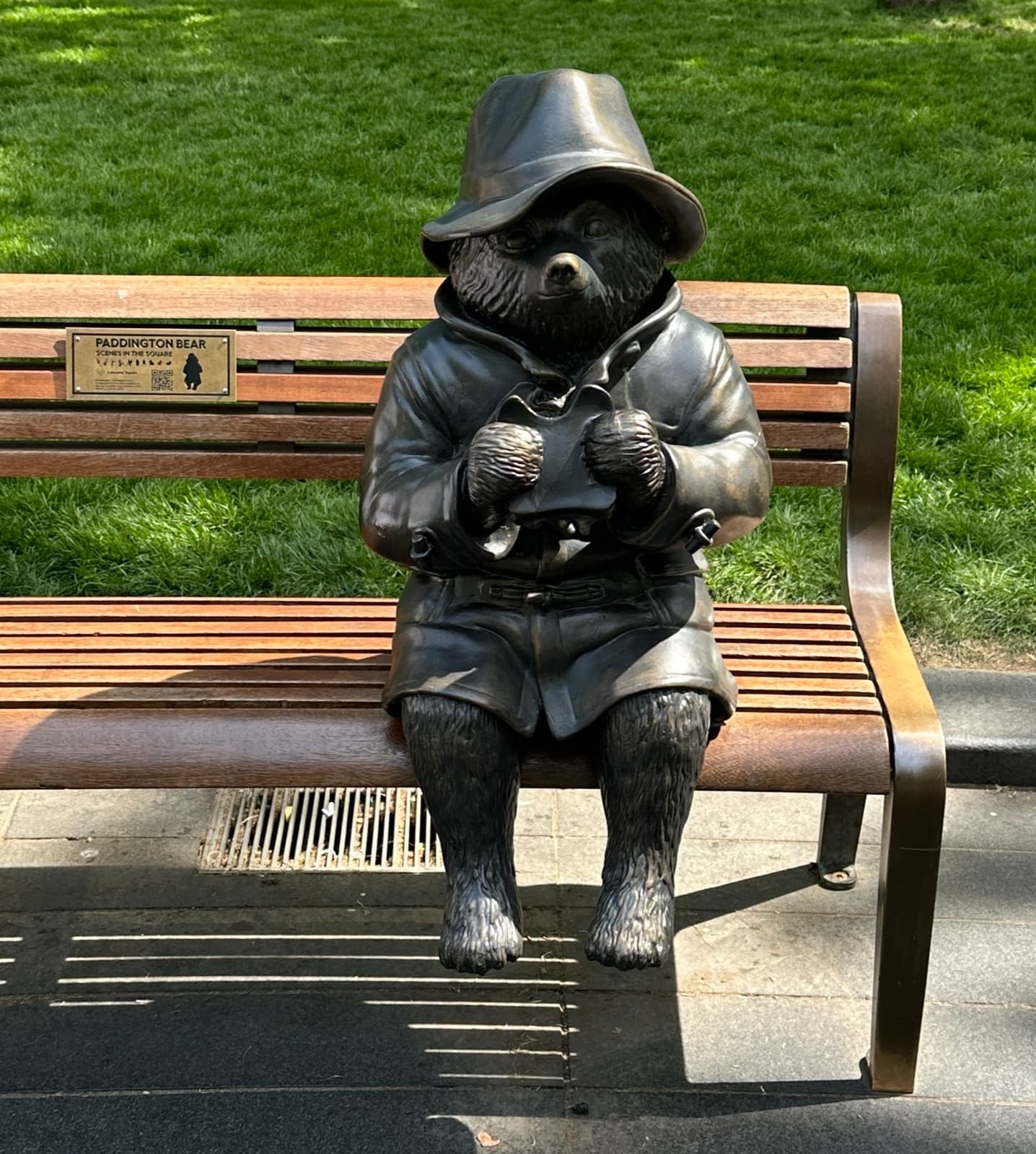A bronze bear statue on a bench in Leicester Square gardens