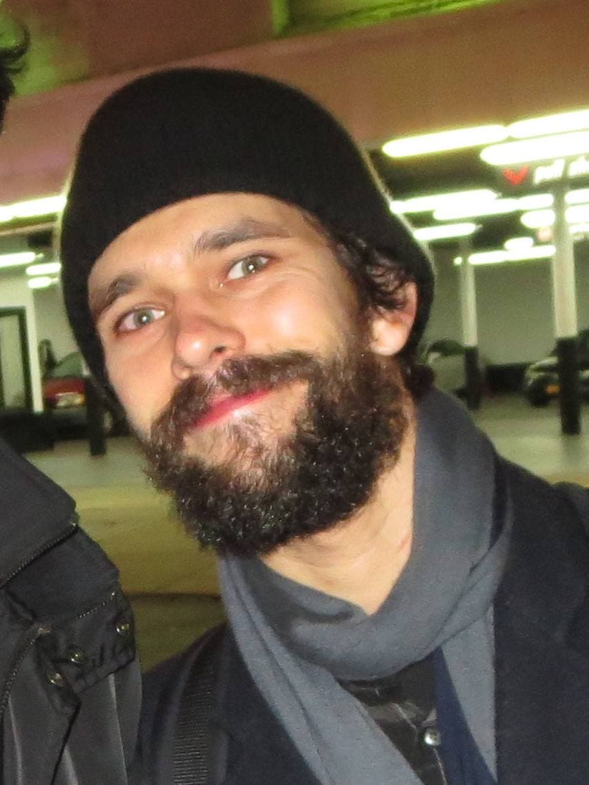 Ben Whishaw in a black beanie and grey scarf, bearded, smiling