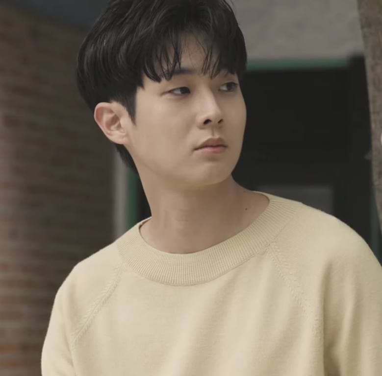 Choi Woo-shik in a cream jumper looking to the side
