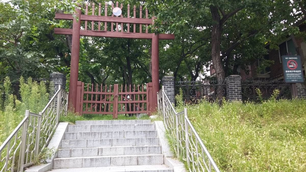 Colour photograph of steps leading up to a red wooden gate among trees