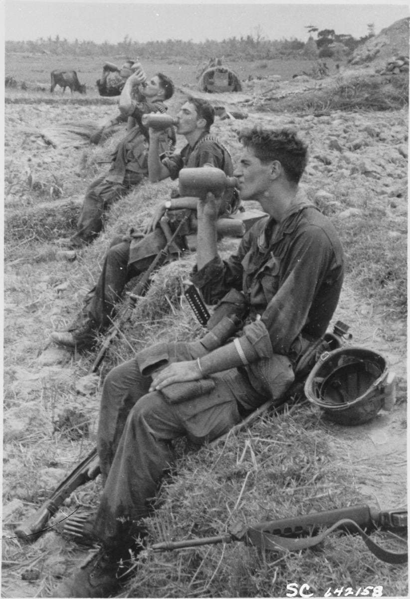 Soldiers resting and drinking from canteens in long grass, 1967