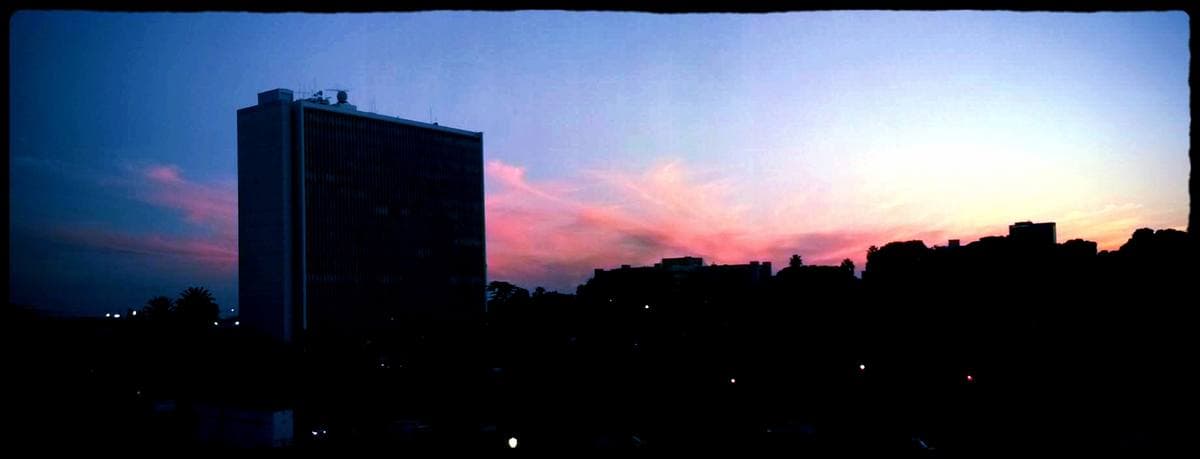 The dark tower of a tall office building against a pink and blue sunset