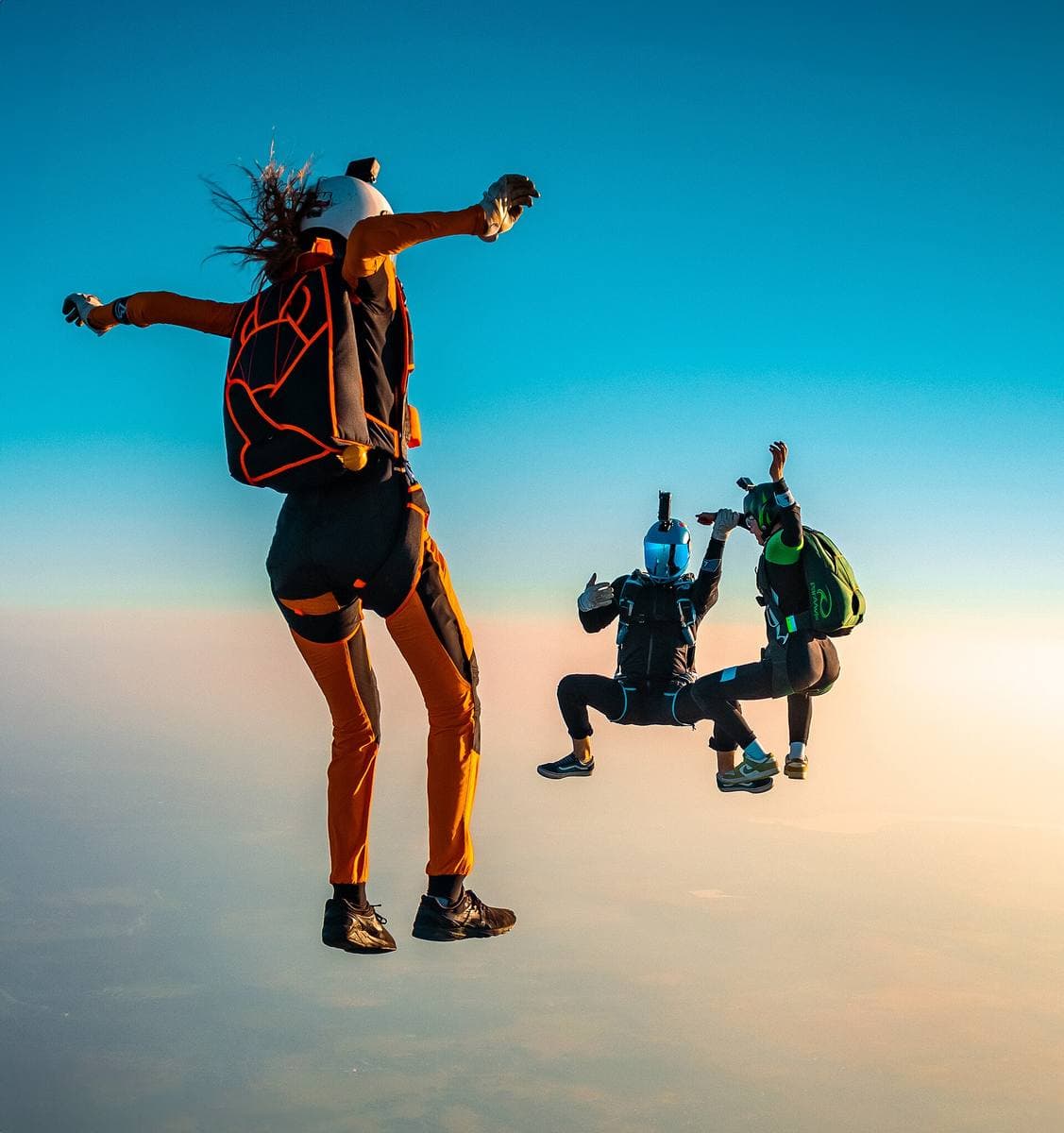 Three skydivers in freefall against a pale orange and blue sky