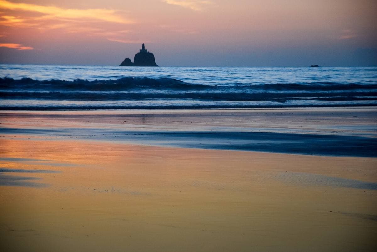 Low sun over a wet beach with surf lines and a sea stack on the horizon