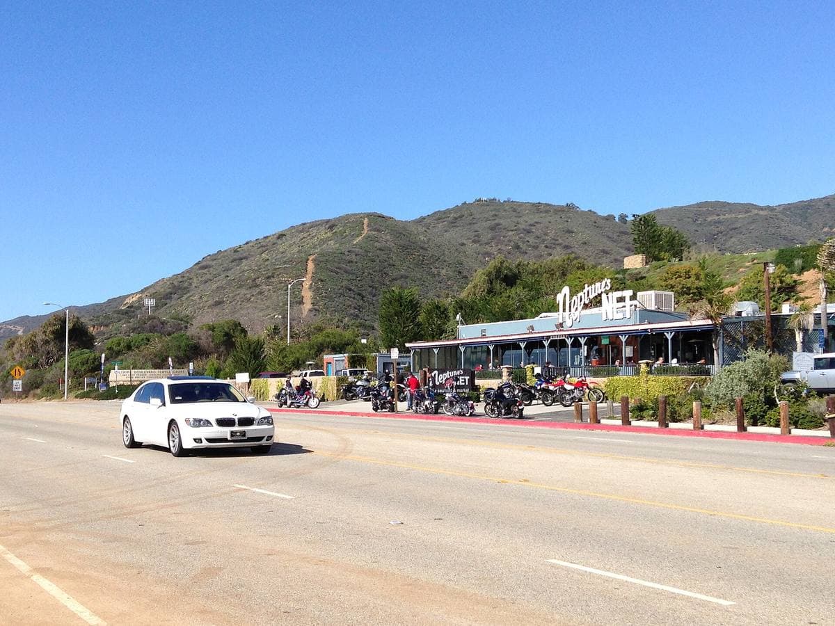 A low seafood shack with a row of motorbikes beside the highway, hills behind
