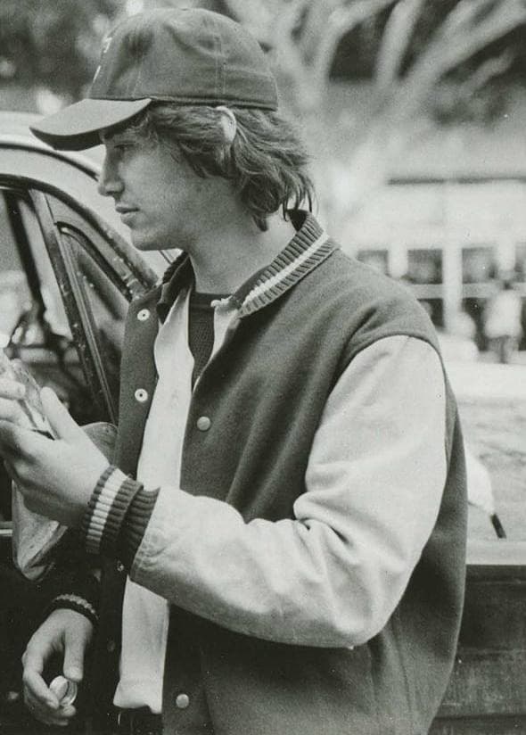 Keanu Reeves aged about 22 in a baseball cap and varsity jacket, in profile