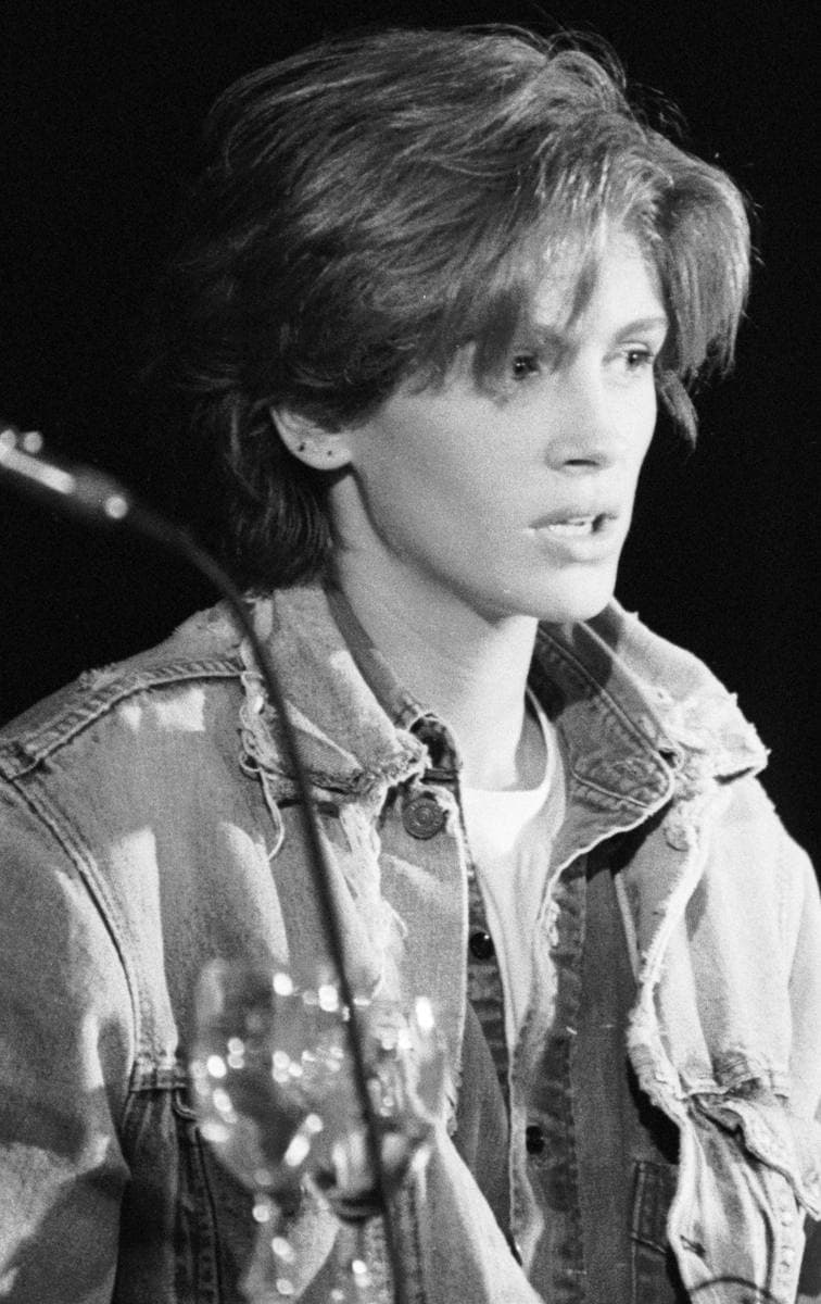 Black-and-white photo of a young Julia Roberts in a denim jacket at a press-conference microphone