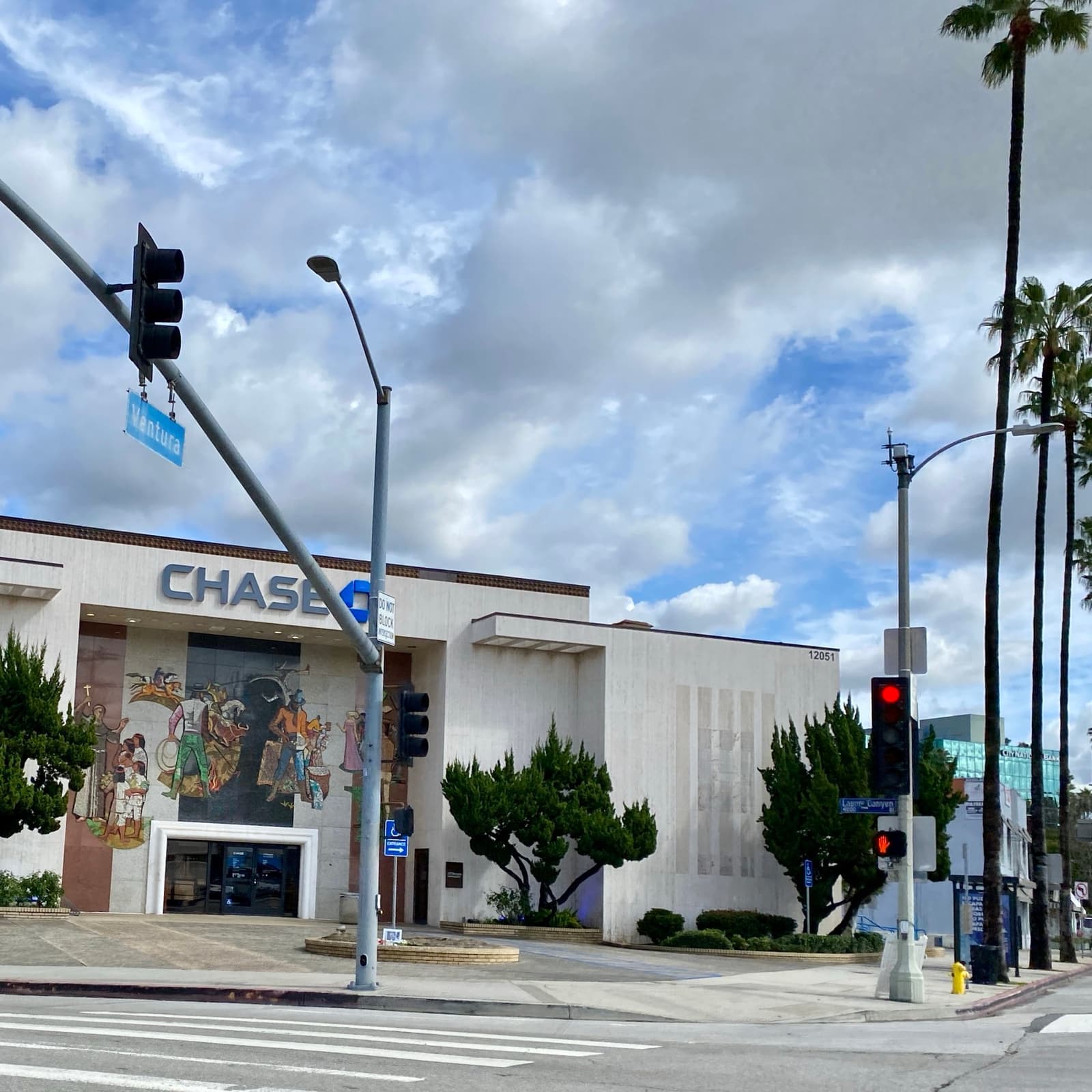 A street corner with a bank and palm trees under clouds