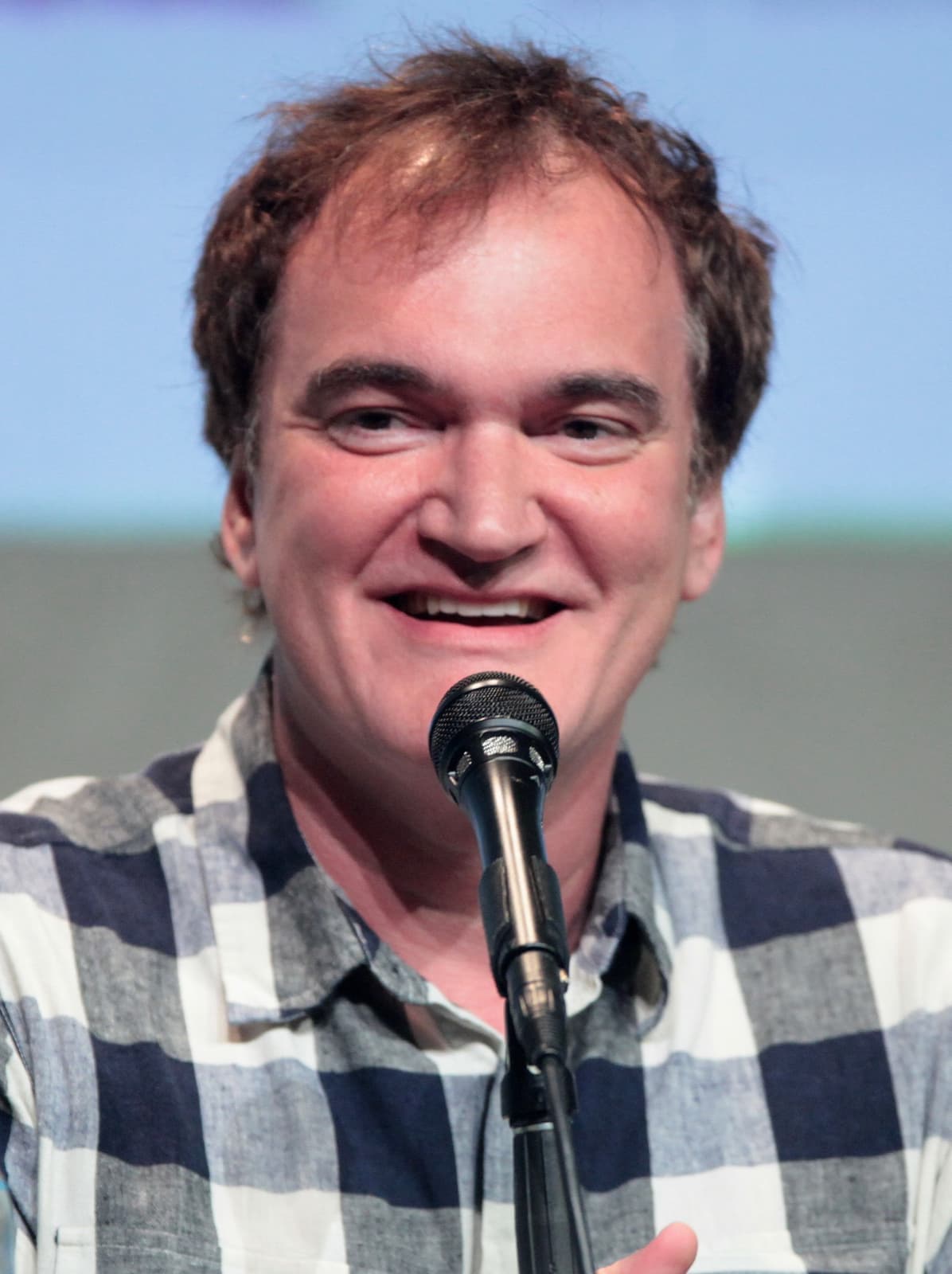 Quentin Tarantino smiling at a microphone, in a checked shirt