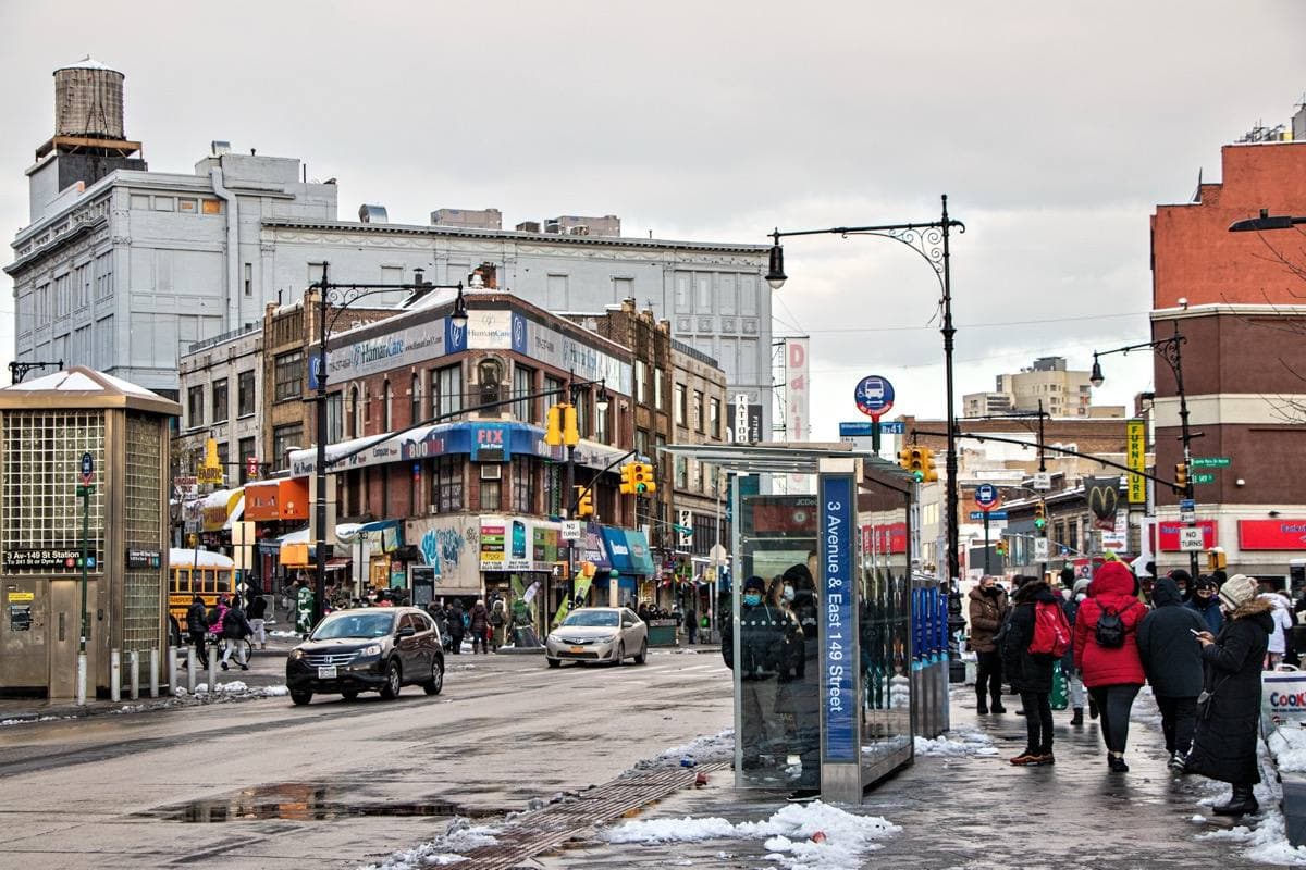 A busy Bronx crossroads with shops, signs and people crossing the street