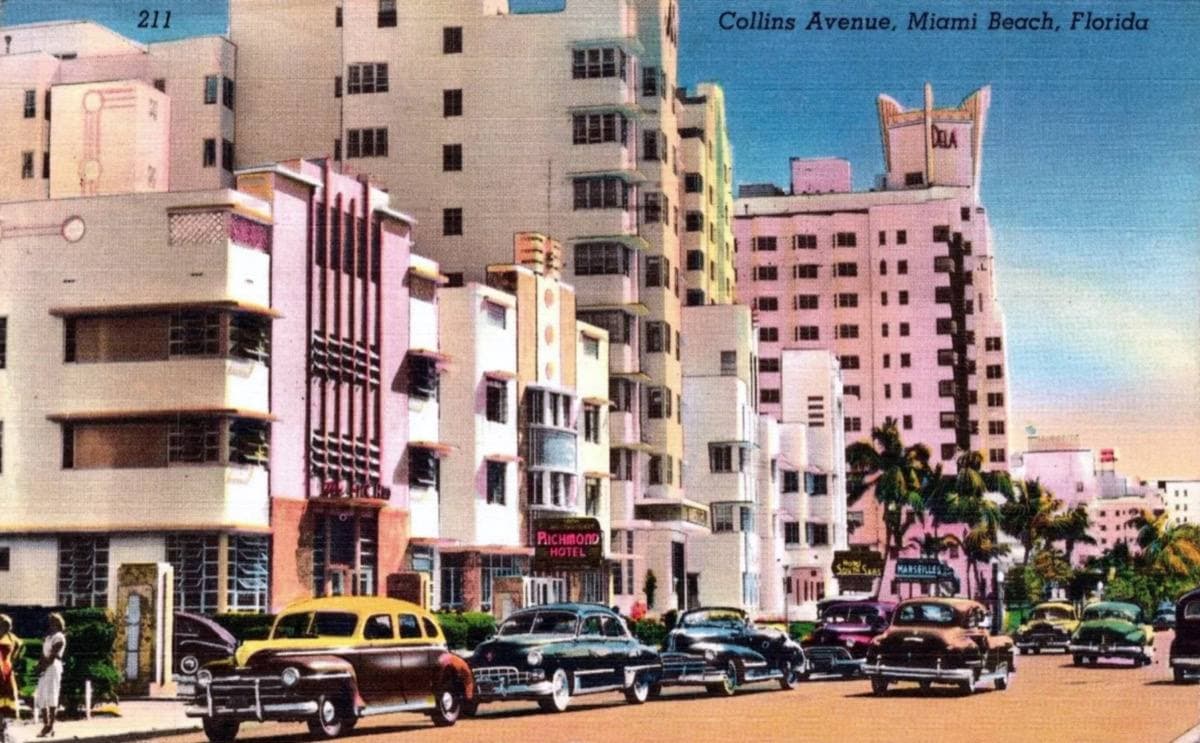 Pastel Art Deco hotels along a palm-lined avenue with 1950s cars