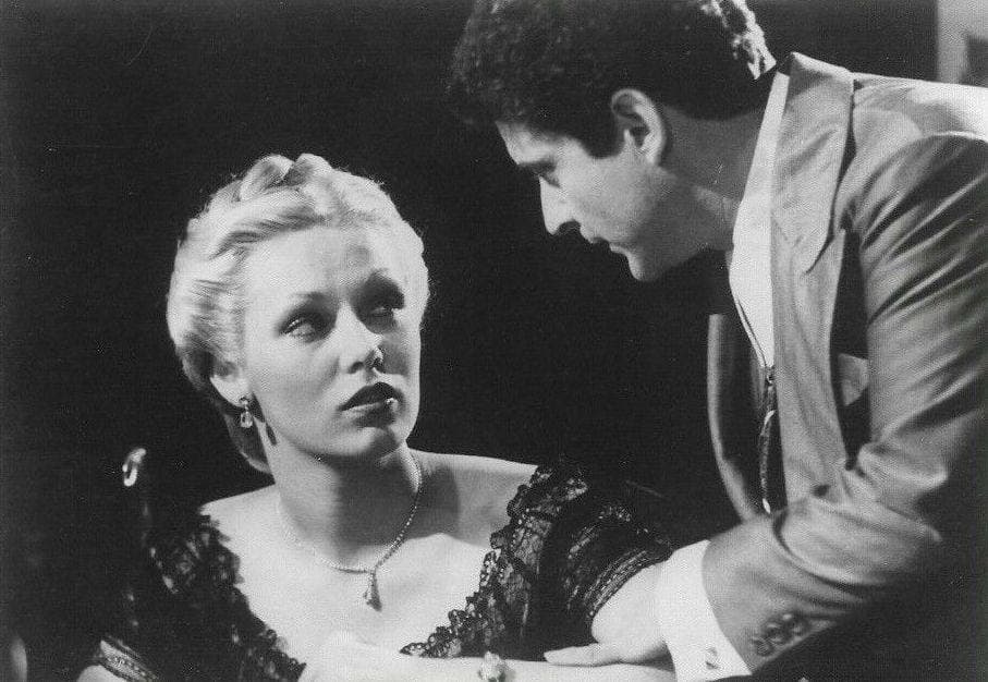 Joe Pesci in a suit leans towards Cathy Moriarty, seated in a lace dress