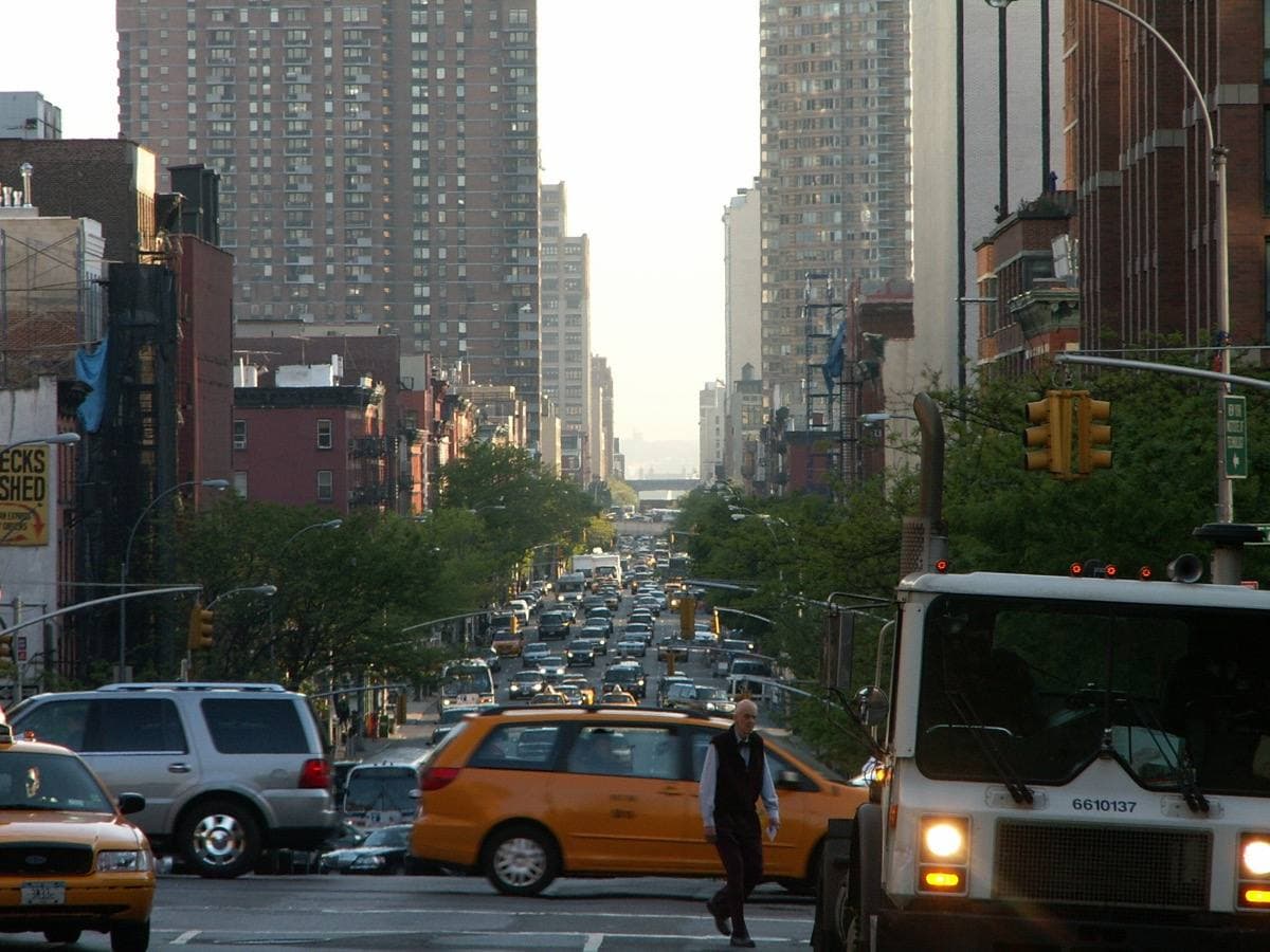 A wide avenue of traffic and yellow cabs running between apartment blocks