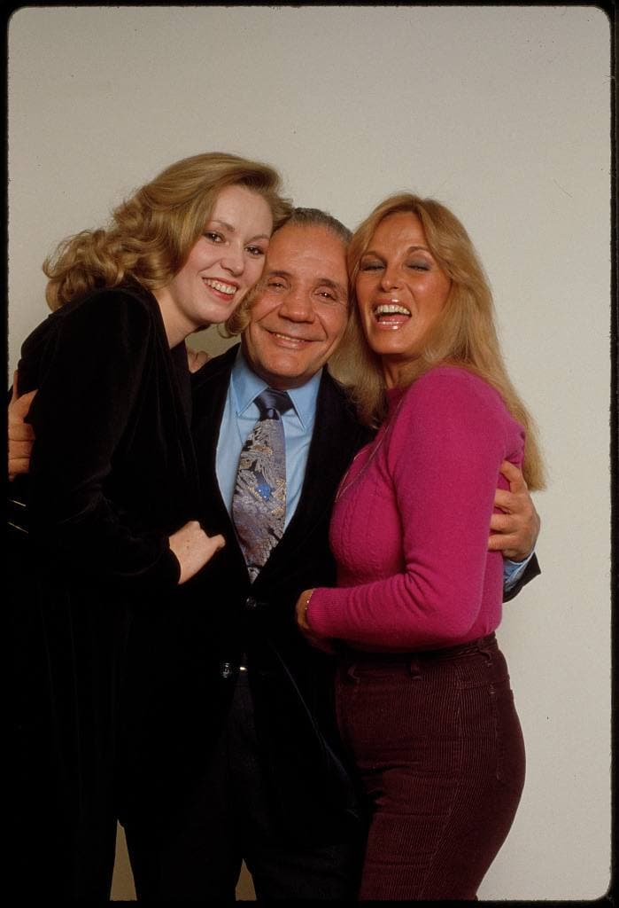 Three people pose together: a young blonde woman in black, Jake LaMotta in a suit, and Vikki LaMotta in a pink jumper