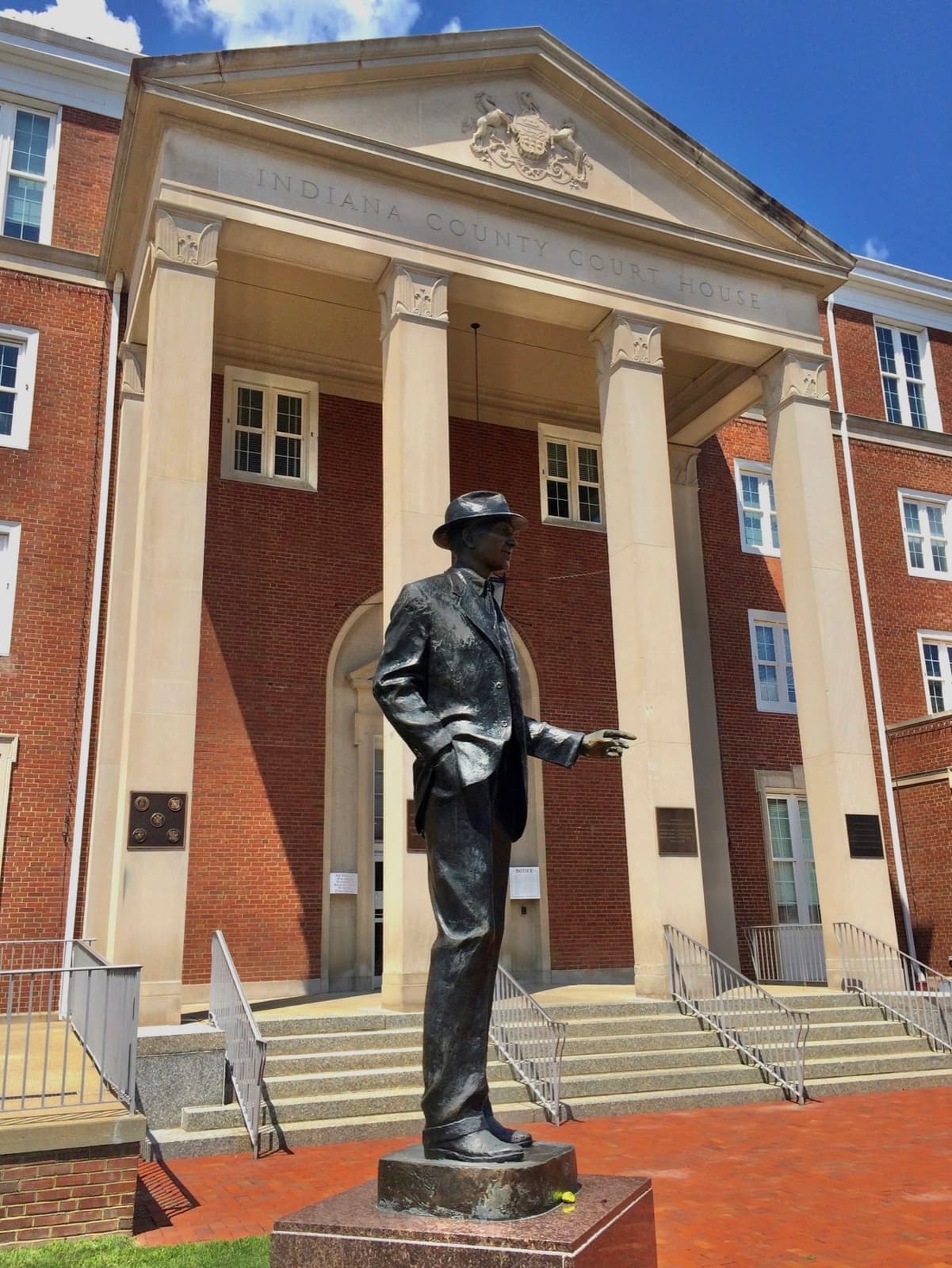 A bronze statue of Jimmy Stewart in front of a brick courthouse with a white clock tower