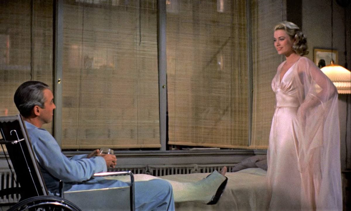 James Stewart in a wheelchair with his leg in plaster, Grace Kelly standing in a pale gown by the bamboo blinds