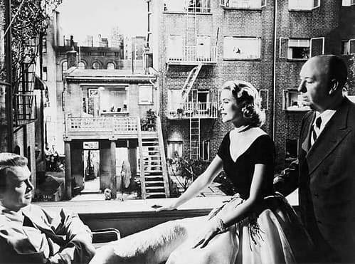 James Stewart in a wheelchair, Grace Kelly and Alfred Hitchcock at an open window, the built courtyard and fire escapes behind them