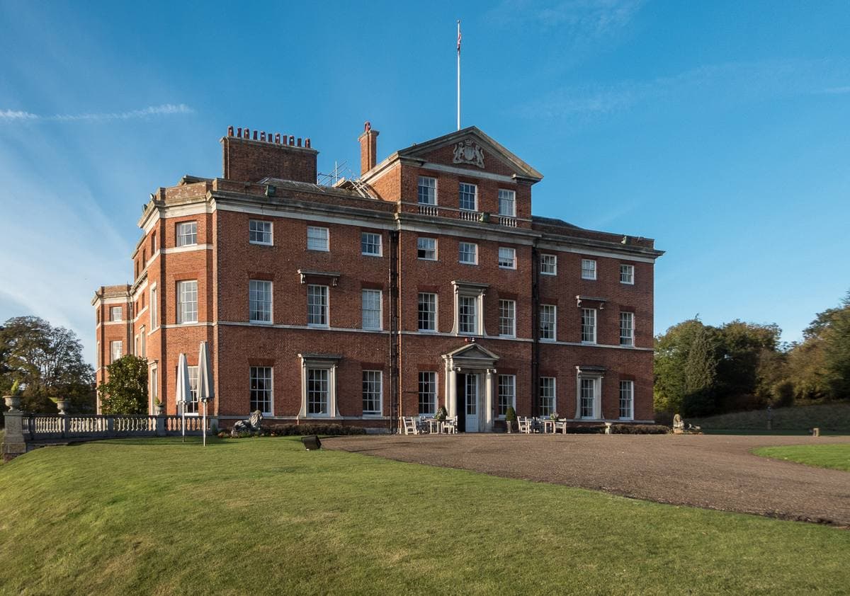 A red-brick Georgian house above a lake in autumn