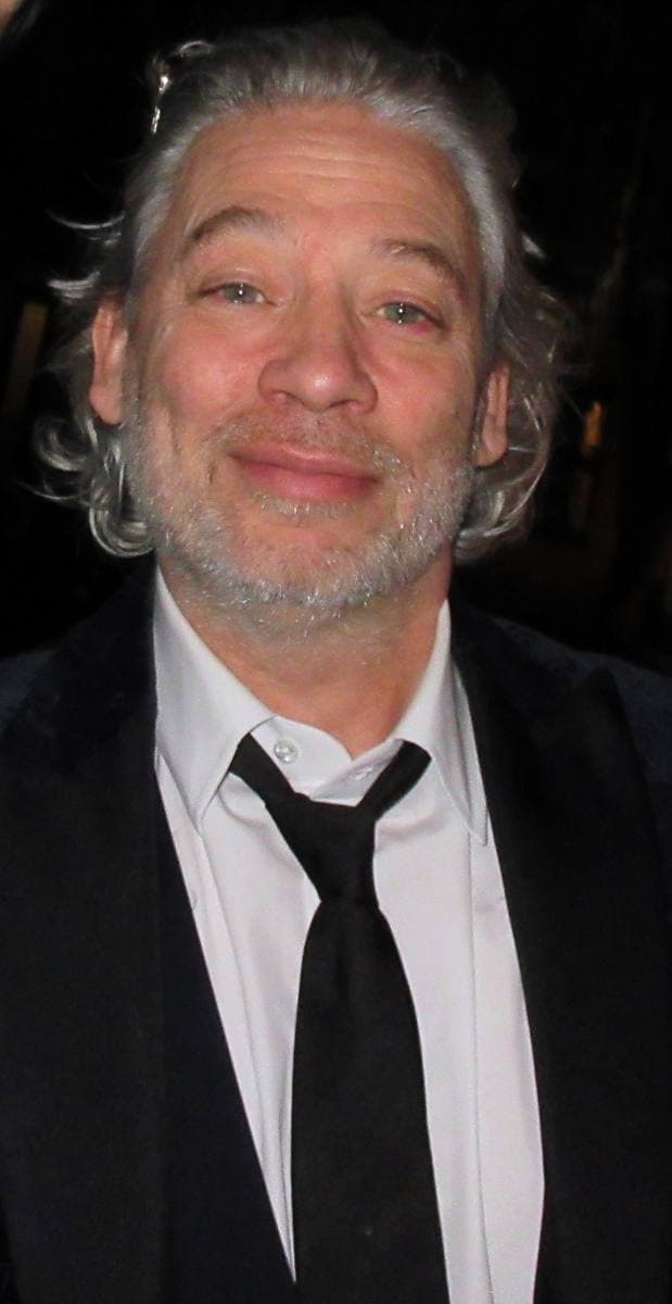 Dexter Fletcher in a dark suit and tie